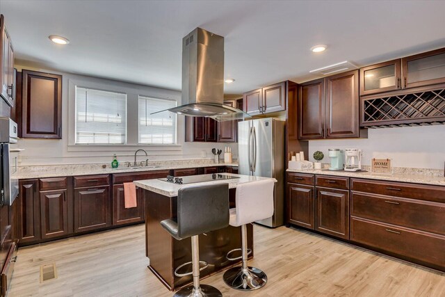 kitchen with light hardwood / wood-style flooring, black electric cooktop, a kitchen island, island exhaust hood, and stainless steel refrigerator