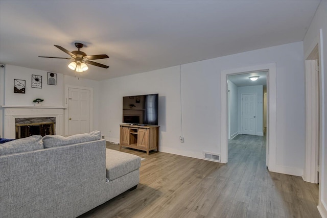 living room with a fireplace, light wood-type flooring, and ceiling fan