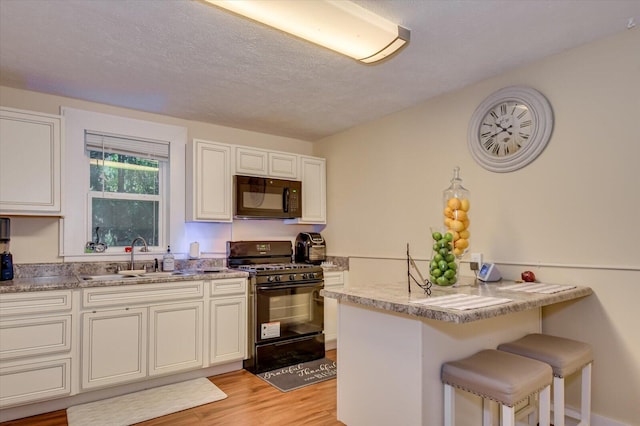 kitchen featuring sink, kitchen peninsula, a breakfast bar, white cabinets, and black appliances