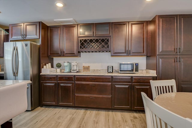 kitchen with dark brown cabinetry, light stone counters, stainless steel appliances, and light wood-type flooring