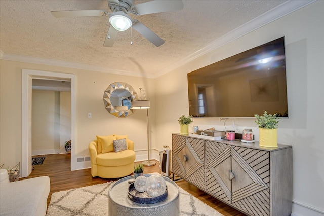 living area with ceiling fan, hardwood / wood-style floors, a textured ceiling, and ornamental molding