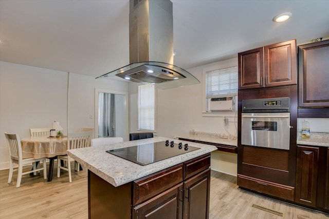 kitchen with island exhaust hood, light wood-type flooring, black electric cooktop, a center island, and oven