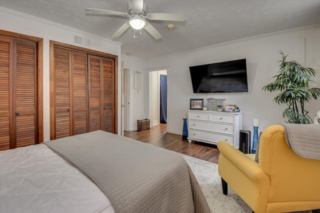 bedroom featuring dark hardwood / wood-style flooring, ornamental molding, a textured ceiling, ceiling fan, and multiple closets