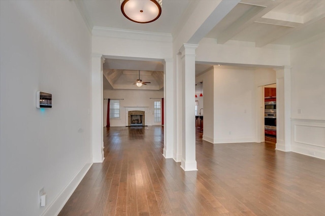 interior space featuring ceiling fan, beam ceiling, a fireplace, dark wood-style floors, and ornate columns