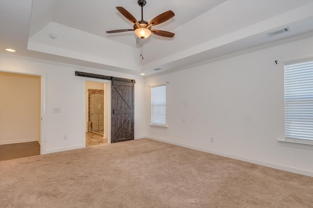 spare room with a tray ceiling, a barn door, visible vents, and carpet floors