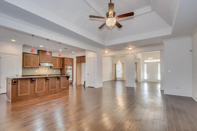 unfurnished living room with crown molding, ceiling fan, a tray ceiling, recessed lighting, and dark wood-style flooring