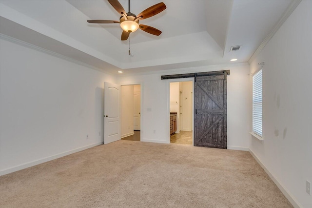 unfurnished bedroom featuring visible vents, crown molding, a barn door, carpet floors, and a raised ceiling