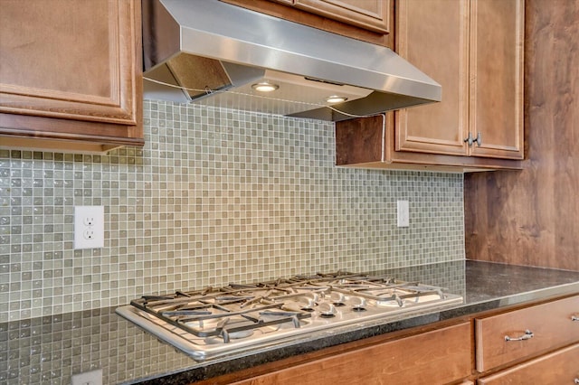 kitchen featuring under cabinet range hood, backsplash, dark countertops, and stainless steel gas stovetop