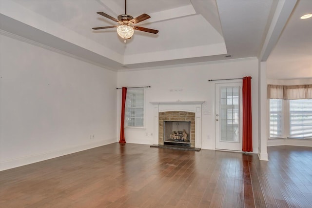 unfurnished living room with a stone fireplace, crown molding, a raised ceiling, ceiling fan, and dark wood-style flooring