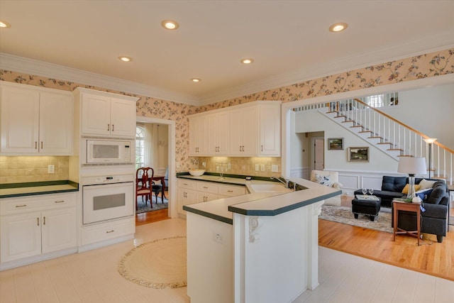 kitchen featuring white cabinetry, backsplash, kitchen peninsula, white appliances, and ornamental molding