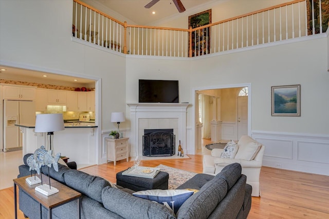 living room featuring light wood-type flooring, a towering ceiling, ornamental molding, ceiling fan, and a tile fireplace