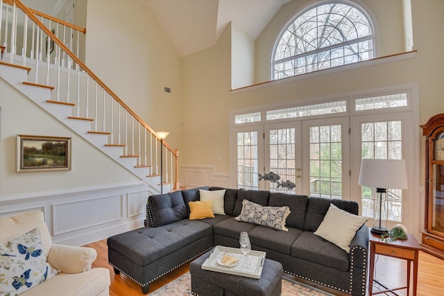 living room featuring french doors, a towering ceiling, and light wood-type flooring