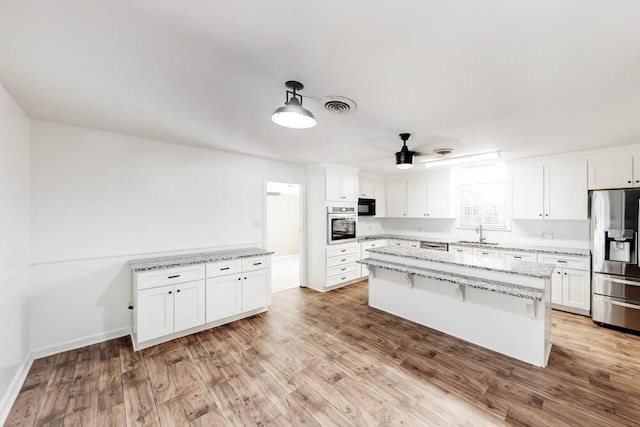 kitchen with white cabinetry, sink, light stone countertops, decorative light fixtures, and appliances with stainless steel finishes