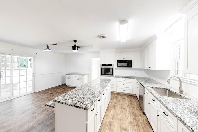 kitchen with appliances with stainless steel finishes, light stone counters, sink, white cabinets, and a center island