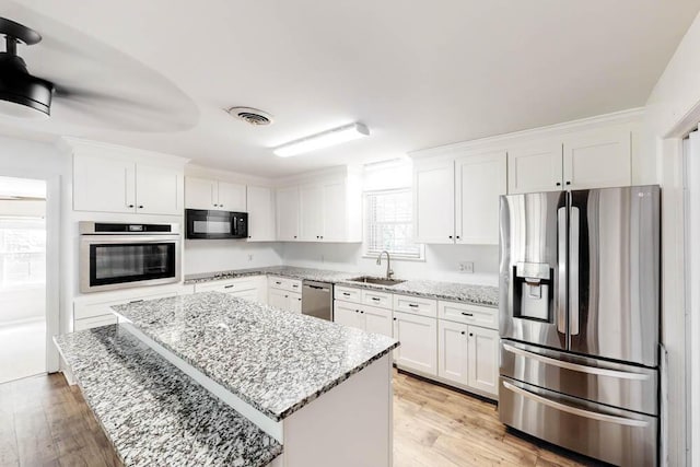 kitchen featuring a center island, white cabinets, sink, light stone countertops, and stainless steel appliances