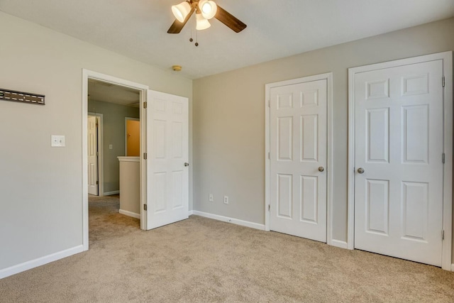 unfurnished bedroom with light colored carpet, ceiling fan, and multiple closets