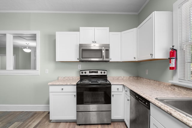 1940 Telfair St, Augusta, GA 30904 - kitchen featuring stainless steel appliances, light wood finished floors, light countertops, white cabinetry, and crown molding
