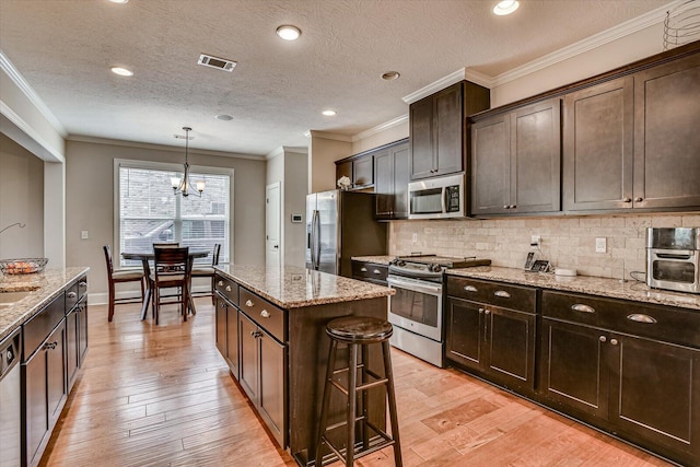 kitchen featuring an inviting chandelier, light stone counters, a kitchen bar, a kitchen island, and appliances with stainless steel finishes