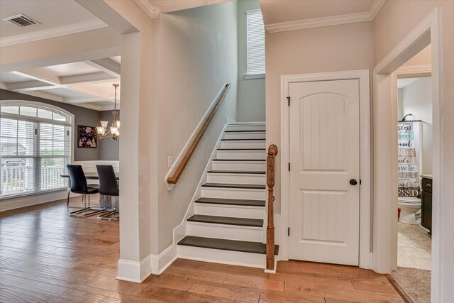 staircase with coffered ceiling, beamed ceiling, a notable chandelier, crown molding, and wood-type flooring