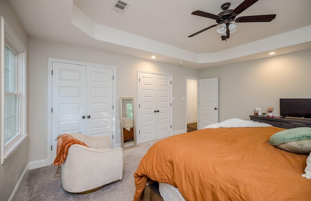 bedroom with carpet flooring, a raised ceiling, ceiling fan, and multiple closets