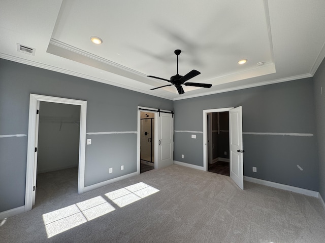 unfurnished bedroom featuring a barn door, a raised ceiling, carpet, a spacious closet, and a closet