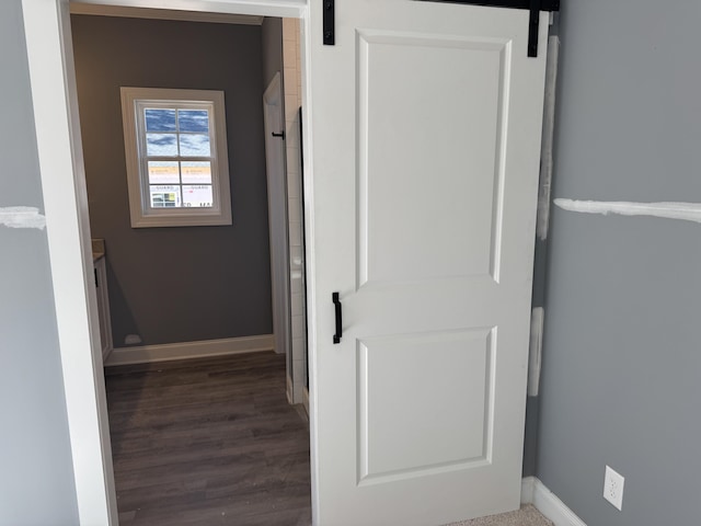 corridor featuring a barn door, baseboards, and wood finished floors