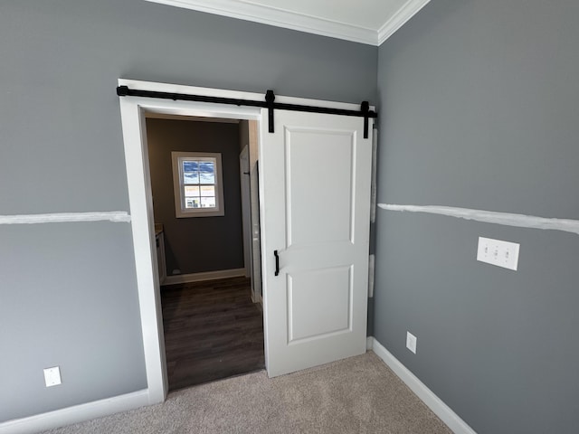 unfurnished bedroom with ornamental molding, carpet flooring, baseboards, and a barn door