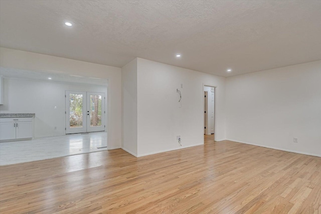 empty room featuring french doors, light wood-type flooring, and a textured ceiling