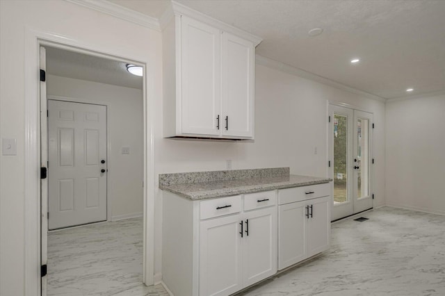 kitchen featuring light stone counters, white cabinetry, crown molding, and french doors