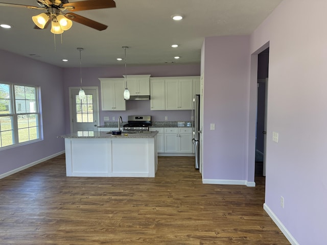 kitchen with an island with sink, stainless steel appliances, hanging light fixtures, and light stone counters