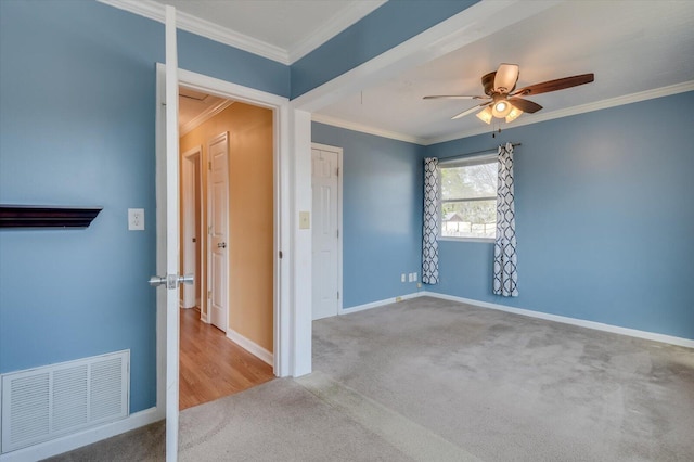 carpeted empty room with visible vents, crown molding, baseboards, and ceiling fan