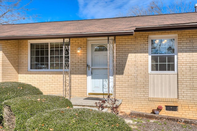 doorway to property featuring a shingled roof, crawl space, and brick siding