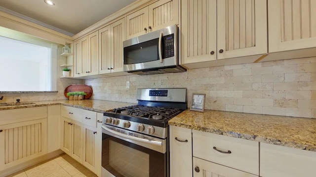 kitchen featuring light stone counters, light tile patterned floors, stainless steel appliances, cream cabinets, and backsplash