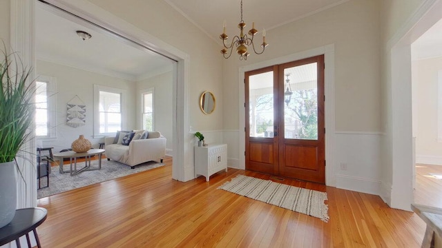 foyer entrance with french doors, ornamental molding, a chandelier, and light hardwood / wood-style floors