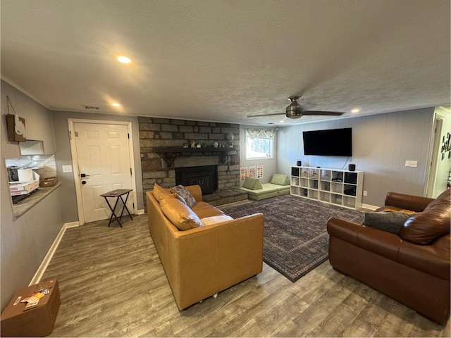 living room with ceiling fan, a stone fireplace, hardwood / wood-style floors, and a textured ceiling