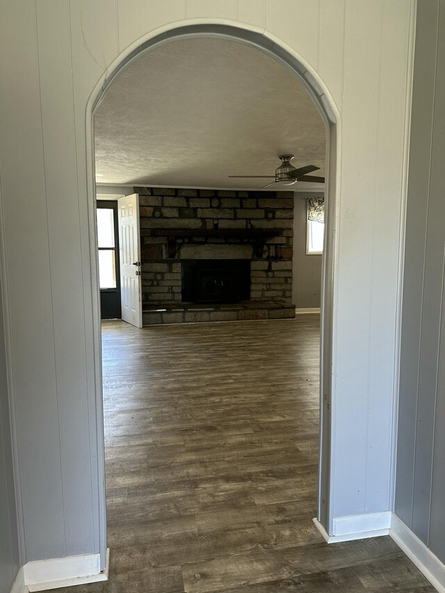 living room with ceiling fan, a stone fireplace, light hardwood / wood-style floors, and a textured ceiling