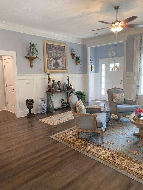 256 Candlewick Loop, Mccormick, SC 29835 - living room with a ceiling fan, crown molding, a decorative wall, dark wood-style flooring, and a wainscoted wall