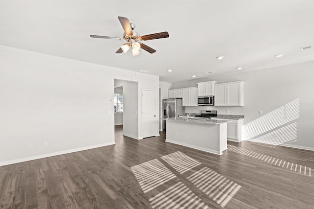 kitchen featuring white cabinetry, stainless steel appliances, dark hardwood / wood-style floors, light stone countertops, and a center island with sink