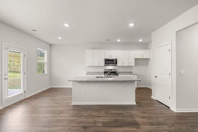 kitchen with light stone countertops, appliances with stainless steel finishes, a kitchen island with sink, and white cabinets