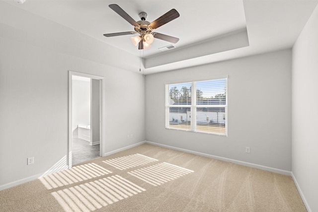 unfurnished bedroom with ceiling fan, light colored carpet, connected bathroom, and a raised ceiling