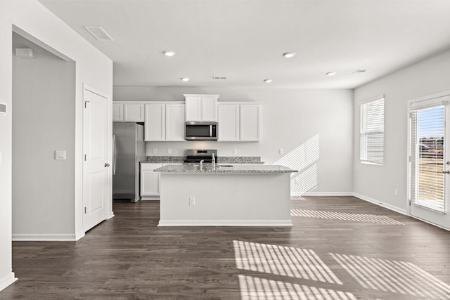 kitchen with a center island with sink, dark hardwood / wood-style floors, stainless steel appliances, light stone countertops, and white cabinets