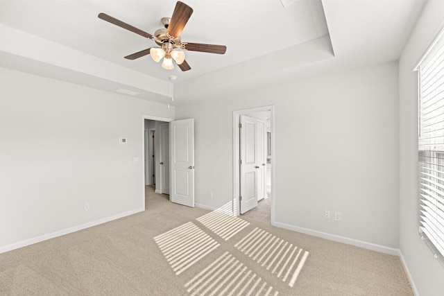 unfurnished bedroom featuring ceiling fan, light colored carpet, a tray ceiling, and ensuite bath