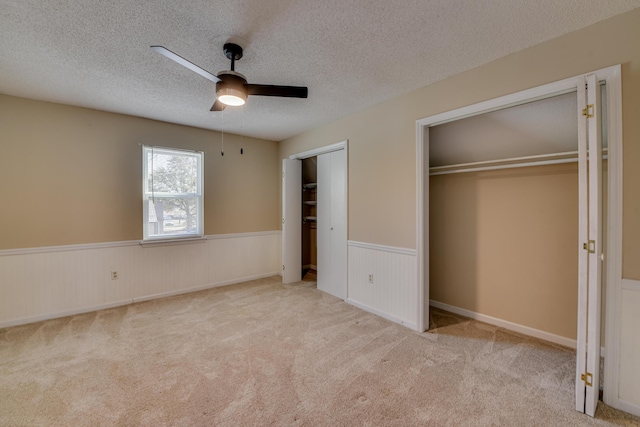 unfurnished bedroom featuring carpet floors, wainscoting, a textured ceiling, and two closets