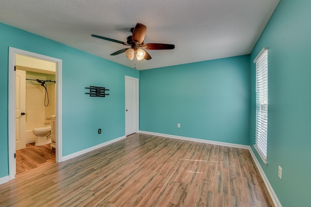 unfurnished bedroom featuring connected bathroom, a textured ceiling, baseboards, and wood finished floors