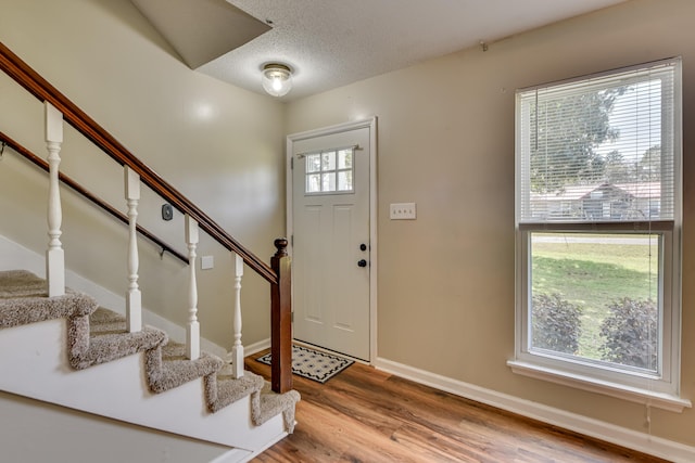 foyer featuring stairway, a textured ceiling, baseboards, and wood finished floors