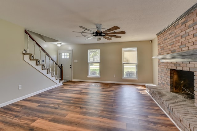 unfurnished living room with dark wood-style flooring, stairway, a brick fireplace, and a wealth of natural light