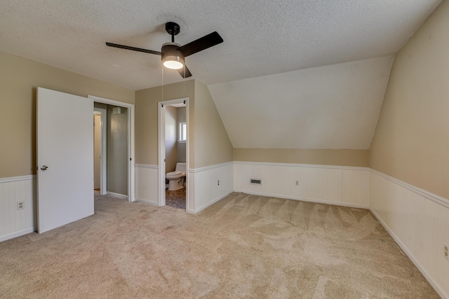 bonus room with lofted ceiling, a textured ceiling, carpet flooring, and wainscoting