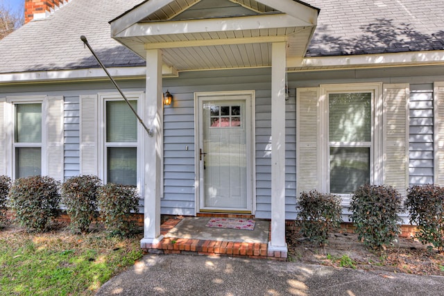 entrance to property featuring a shingled roof and a chimney