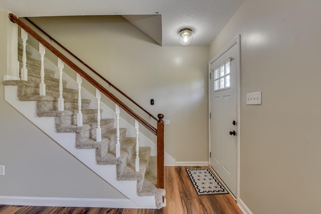 foyer entrance with stairway, a textured ceiling, baseboards, and wood finished floors