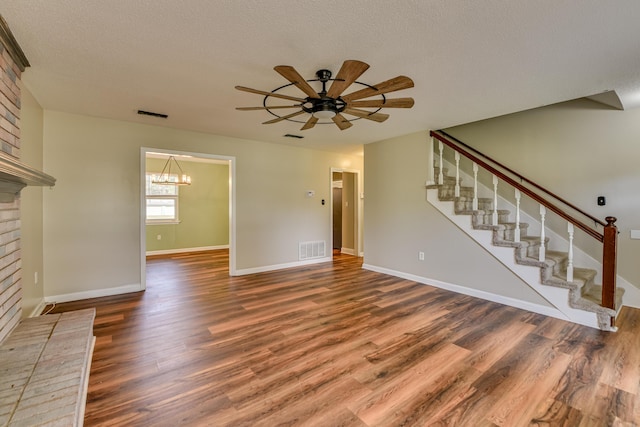 unfurnished living room featuring ceiling fan with notable chandelier, visible vents, stairway, and wood finished floors